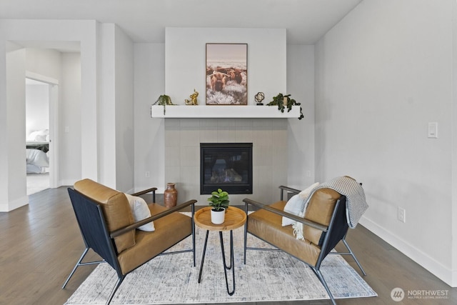 living area with a tiled fireplace, baseboards, and wood finished floors