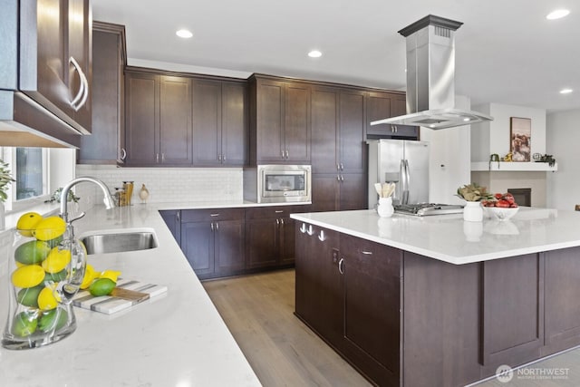 kitchen with tasteful backsplash, appliances with stainless steel finishes, island exhaust hood, light wood-type flooring, and a sink