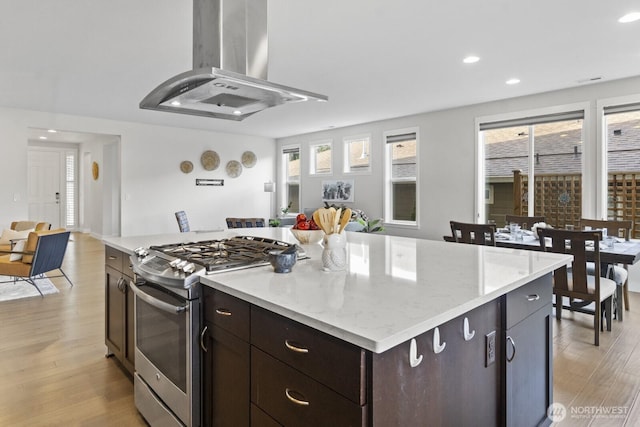 kitchen with stainless steel gas range oven, a kitchen island, open floor plan, light wood-type flooring, and island exhaust hood