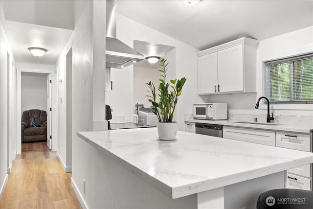 kitchen featuring white microwave, a sink, white cabinetry, dishwasher, and wall chimney exhaust hood