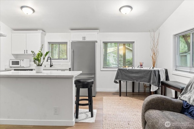 kitchen with white microwave, freestanding refrigerator, light countertops, white cabinetry, and a sink