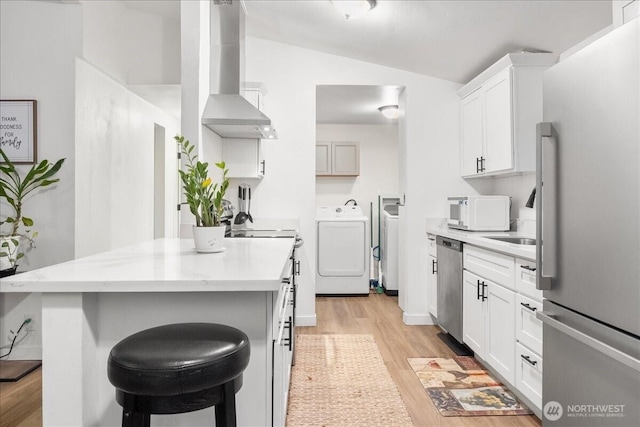 kitchen featuring wall chimney exhaust hood, appliances with stainless steel finishes, vaulted ceiling, light wood-style floors, and washing machine and dryer