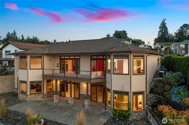 back of property at dusk featuring stone siding, a patio, a balcony, and central air condition unit