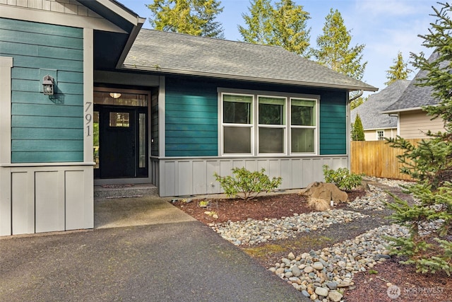 property entrance with board and batten siding, fence, and a shingled roof