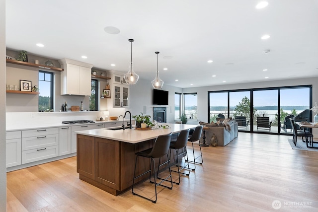 kitchen with an island with sink, light wood-style flooring, light countertops, stainless steel gas stovetop, and a sink