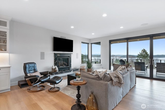 living area with baseboards, a premium fireplace, light wood-style flooring, and recessed lighting