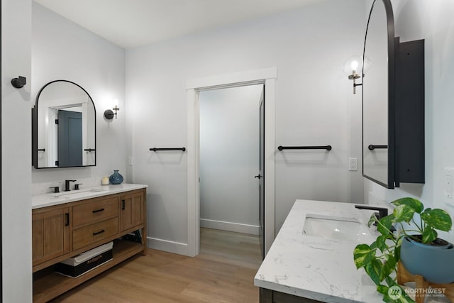 bathroom featuring wood finished floors, two vanities, a sink, and baseboards