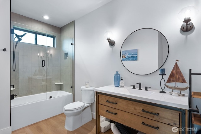 full bathroom featuring toilet, shower / bath combination with glass door, wood finished floors, and vanity