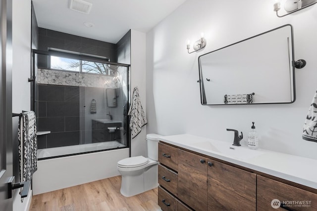 full bathroom with visible vents, toilet, enclosed tub / shower combo, vanity, and wood finished floors