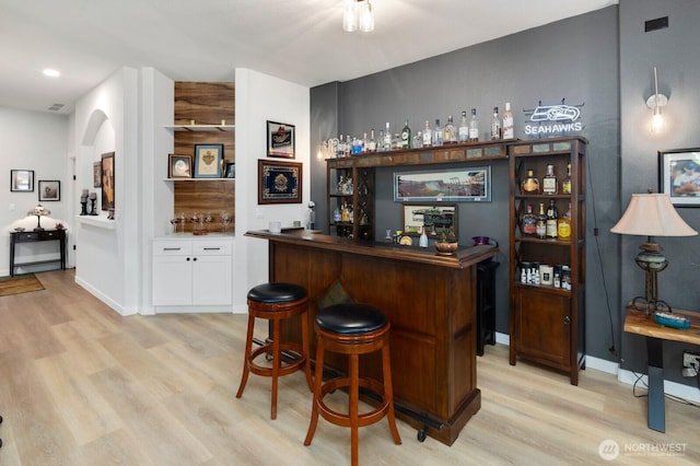 bar with a dry bar, light wood-type flooring, arched walkways, and baseboards