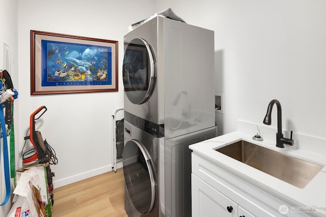 laundry area featuring stacked washer and dryer, a sink, baseboards, light wood-type flooring, and cabinet space