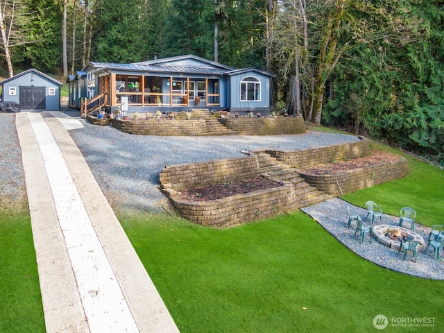 view of front of home with an outdoor fire pit, covered porch, concrete driveway, a front lawn, and a standing seam roof