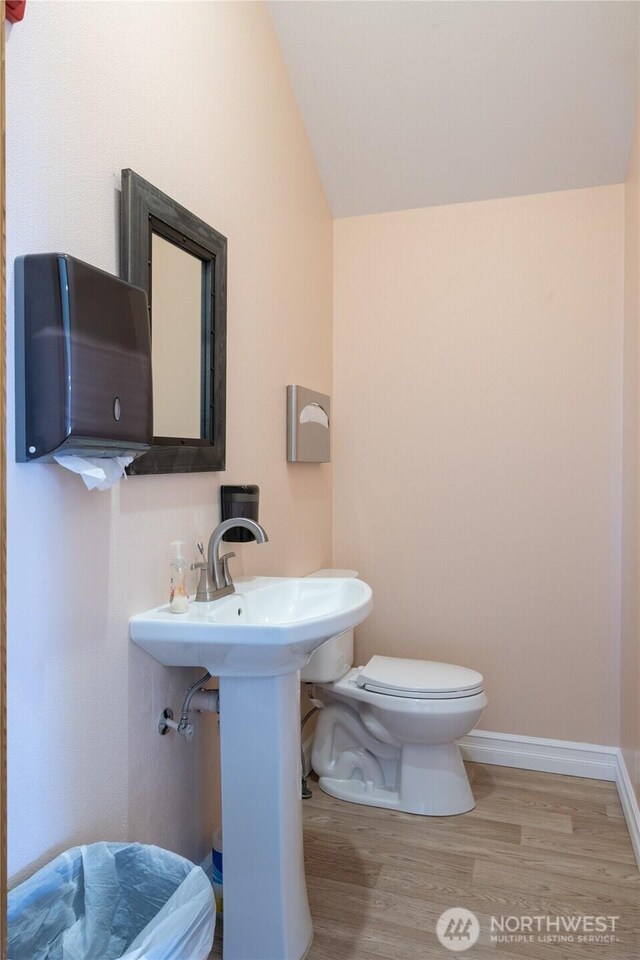 half bathroom featuring lofted ceiling, baseboards, toilet, and wood finished floors
