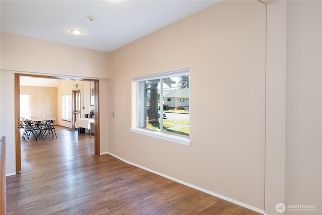 hall featuring baseboards, wood finished floors, and a healthy amount of sunlight