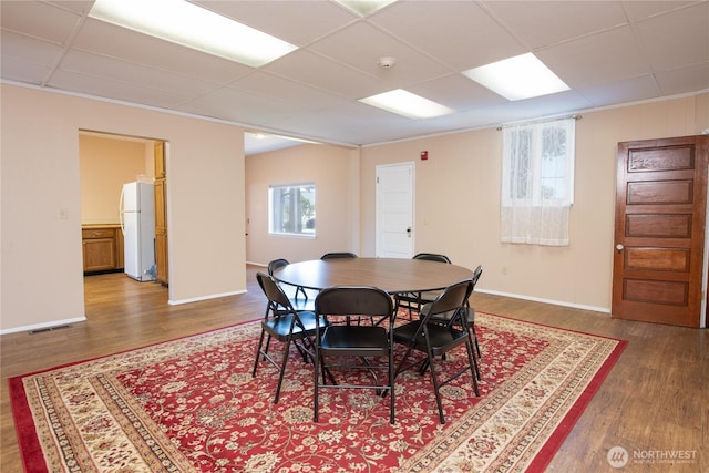 dining room featuring baseboards, visible vents, a drop ceiling, and wood finished floors