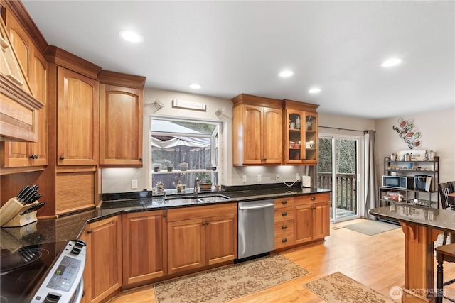 kitchen with dark stone counters, light wood-style flooring, a sink, stainless steel appliances, and glass insert cabinets