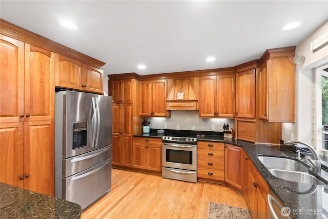 kitchen featuring brown cabinetry, light wood-style floors, custom exhaust hood, stainless steel appliances, and a sink