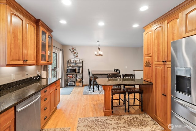 kitchen with light wood-type flooring, a breakfast bar, dark stone counters, appliances with stainless steel finishes, and glass insert cabinets