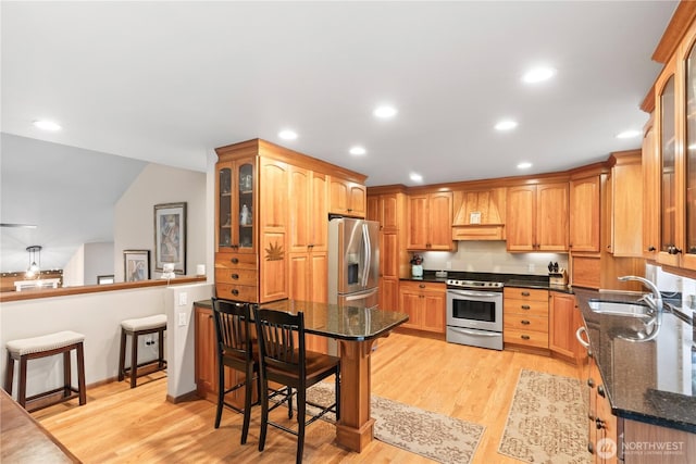 kitchen with a breakfast bar, a peninsula, light wood-type flooring, and appliances with stainless steel finishes