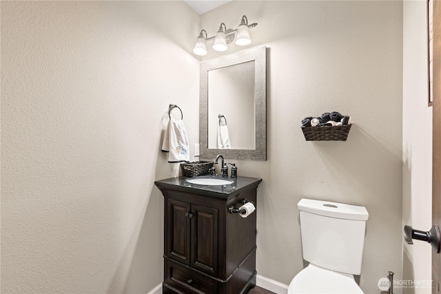 half bathroom with vanity, toilet, and baseboards