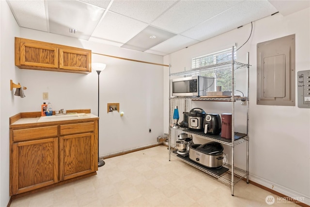 kitchen featuring light floors, electric panel, a sink, stainless steel microwave, and brown cabinets