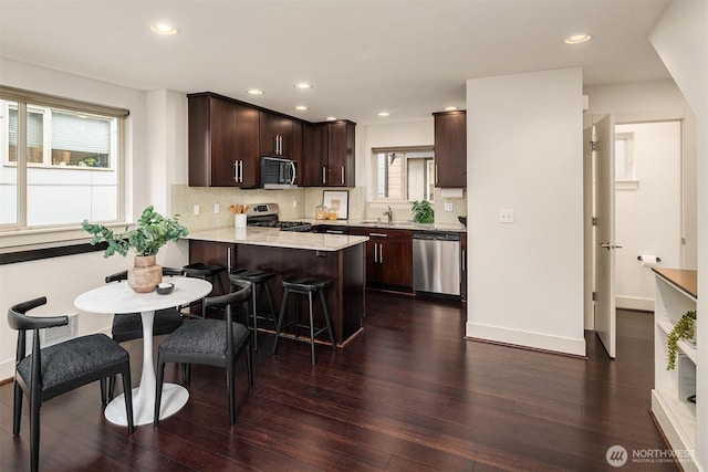 kitchen with dark brown cabinetry, dark wood-style floors, appliances with stainless steel finishes, a peninsula, and a sink