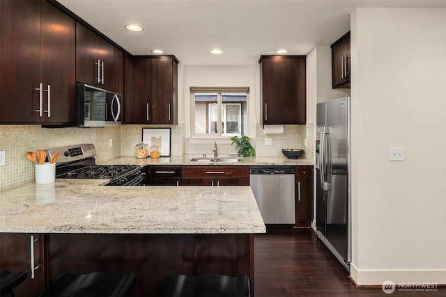 kitchen with light stone counters, stainless steel appliances, a breakfast bar, a peninsula, and a sink