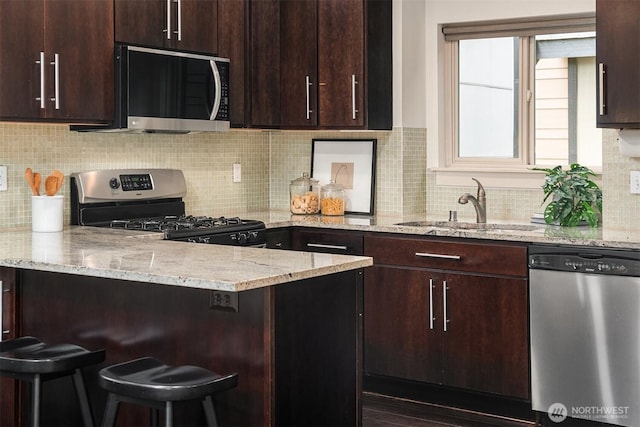 kitchen with light stone countertops, appliances with stainless steel finishes, dark brown cabinets, and a sink