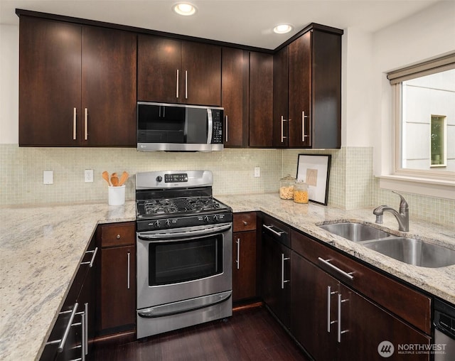 kitchen with dark wood-style floors, stainless steel appliances, dark brown cabinetry, a sink, and light stone countertops