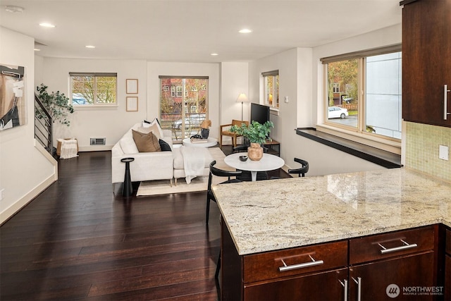 kitchen featuring dark wood-style flooring, visible vents, decorative backsplash, open floor plan, and light stone countertops