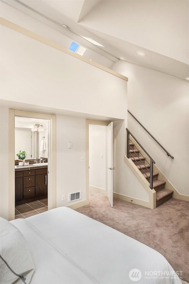 bedroom featuring light carpet, visible vents, baseboards, ensuite bath, and high vaulted ceiling