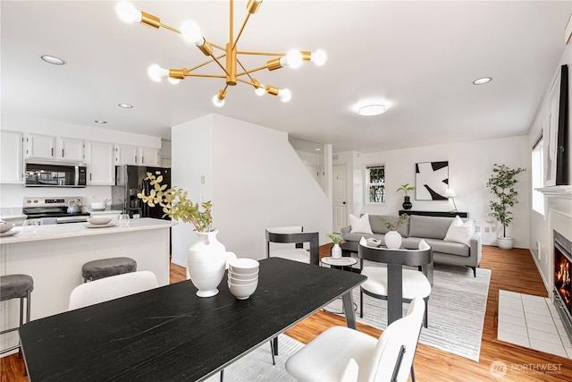 dining area featuring a fireplace with flush hearth, recessed lighting, a chandelier, and light wood-style floors