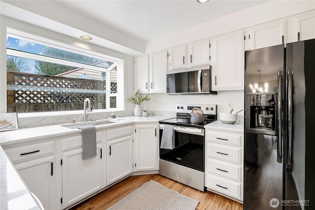 kitchen featuring light wood finished floors, appliances with stainless steel finishes, light countertops, white cabinetry, and a sink