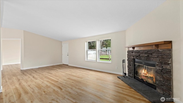 unfurnished living room with a stone fireplace, baseboards, and wood finished floors