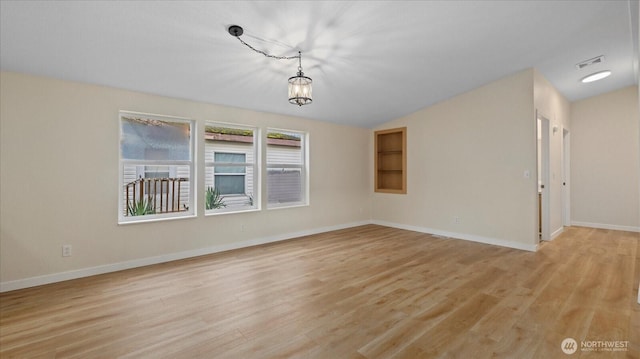 empty room with a notable chandelier, lofted ceiling, visible vents, light wood-type flooring, and baseboards