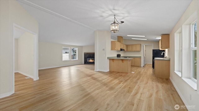 kitchen with light wood finished floors, lofted ceiling, open floor plan, light brown cabinetry, and a fireplace