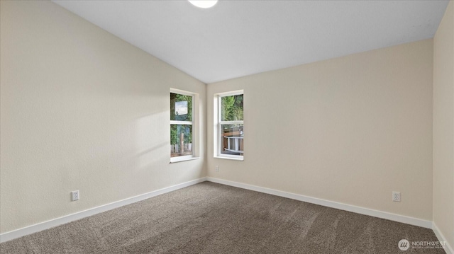 spare room with lofted ceiling, dark carpet, and baseboards