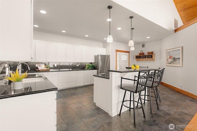 kitchen featuring white cabinets, dark countertops, freestanding refrigerator, a sink, and backsplash