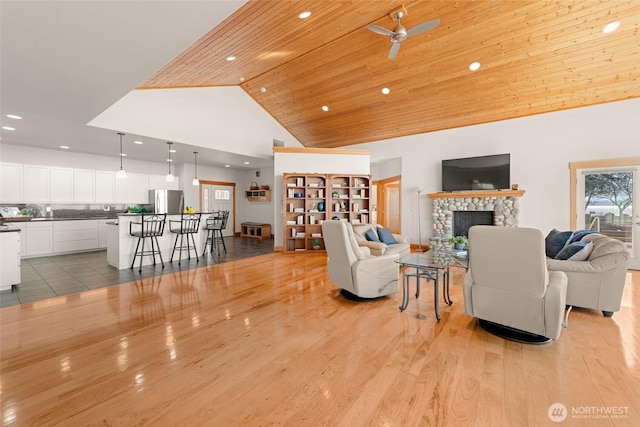 living area featuring ceiling fan, high vaulted ceiling, wooden ceiling, light wood-style flooring, and a tiled fireplace