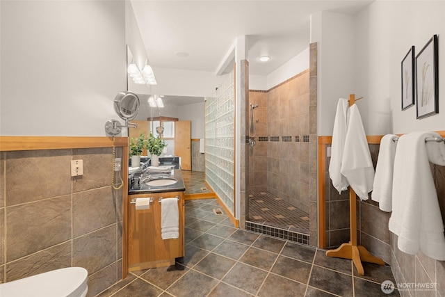 full bathroom featuring toilet, vanity, tile walls, tile patterned floors, and a stall shower