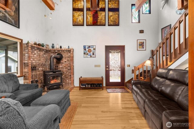 living room with stairs, a wood stove, a towering ceiling, and light wood finished floors