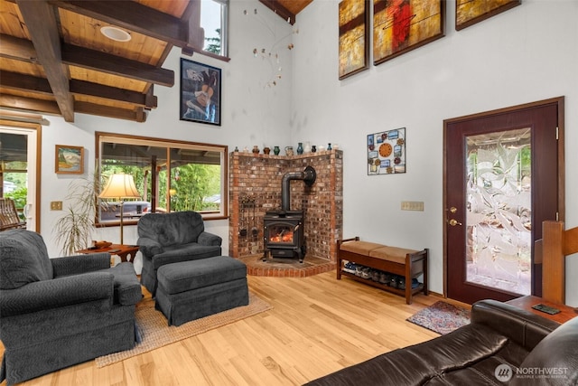 living room with a wealth of natural light, beamed ceiling, a wood stove, and wood finished floors