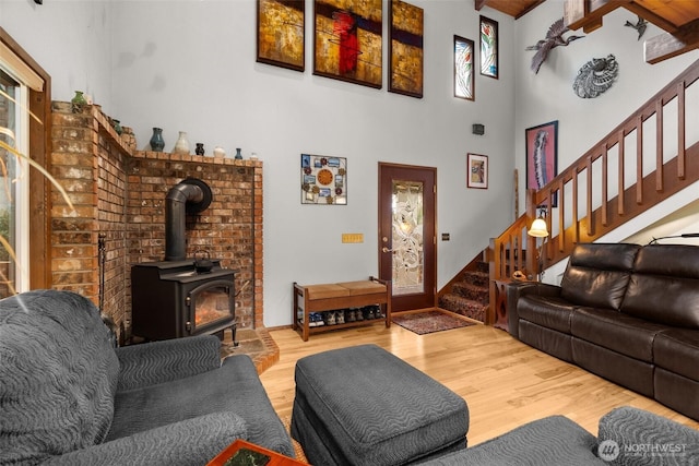 living room featuring a towering ceiling, stairs, a wood stove, and wood finished floors