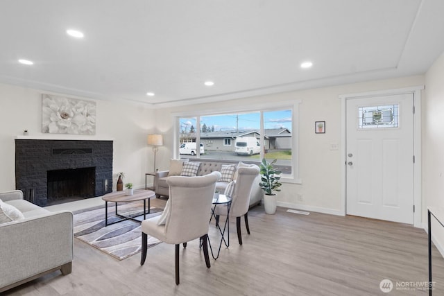 living room featuring baseboards, a fireplace with raised hearth, wood finished floors, and recessed lighting