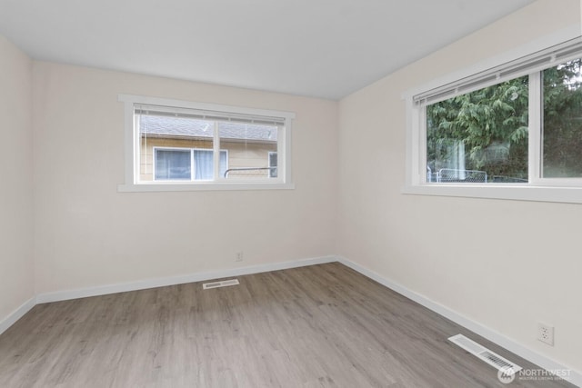 spare room featuring wood finished floors, visible vents, and baseboards