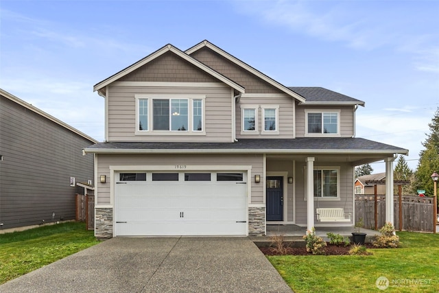 craftsman-style home with fence, a porch, concrete driveway, a front yard, and stone siding