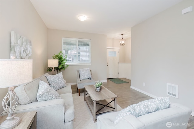 living room with light wood-type flooring, visible vents, baseboards, and an inviting chandelier