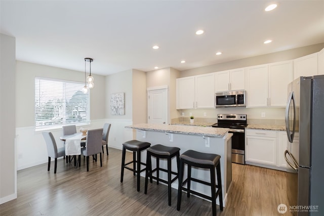 kitchen with light stone countertops, a breakfast bar area, appliances with stainless steel finishes, wood finished floors, and white cabinets
