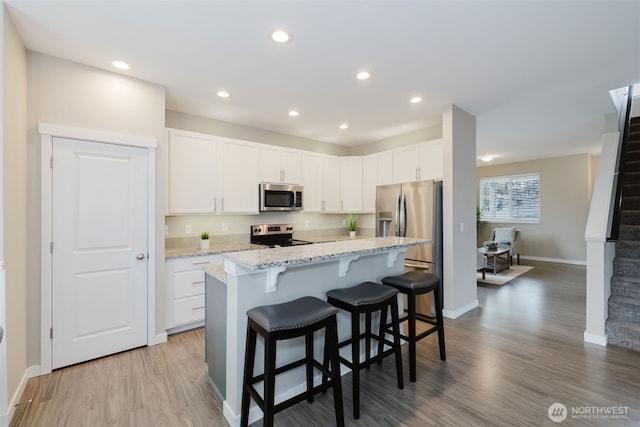 kitchen with white cabinetry, a breakfast bar area, wood finished floors, and appliances with stainless steel finishes