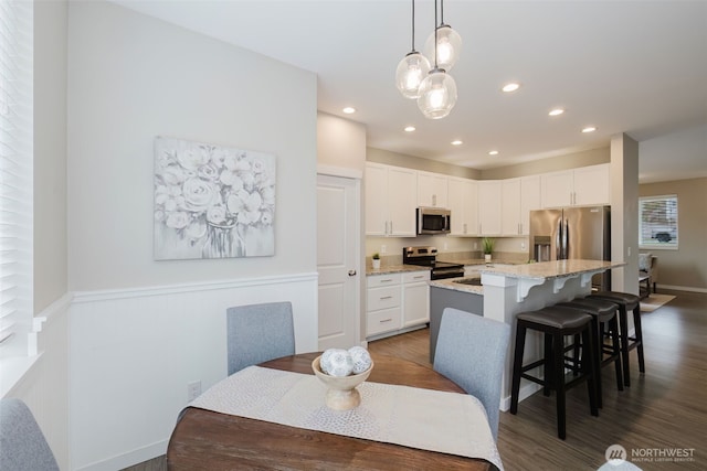 kitchen featuring white cabinetry, a kitchen breakfast bar, stainless steel appliances, and dark wood-style flooring